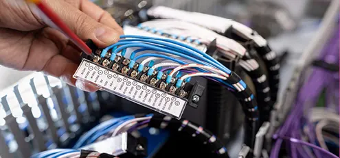 Close-up of a technician’s hand arranging labelled network or control cables in a service panel.