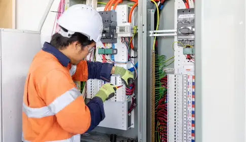 Electrician in high‑visibility gear working inside an electrical control panel.