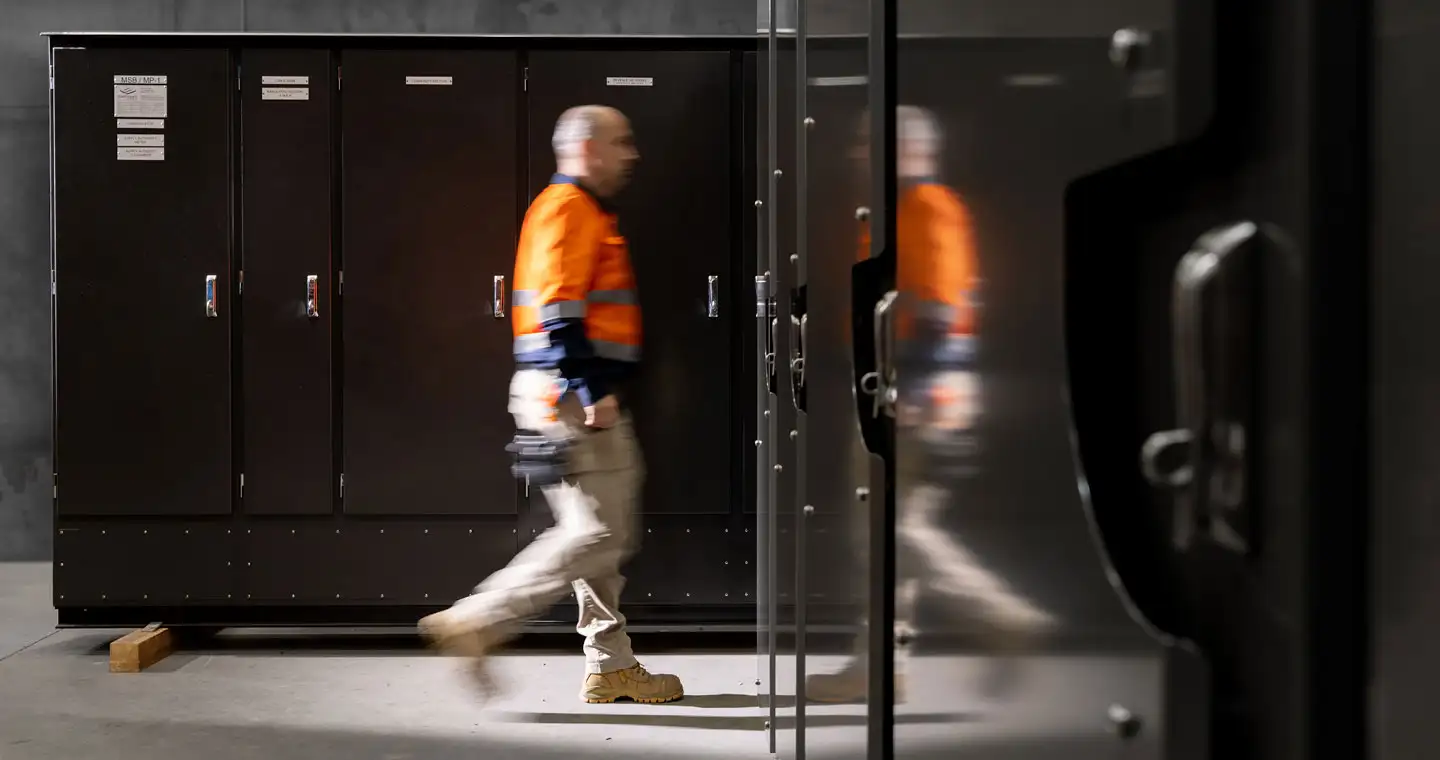 Electrician walking past and inspecting electrical switchboards for commercial electrical and data services in Australia